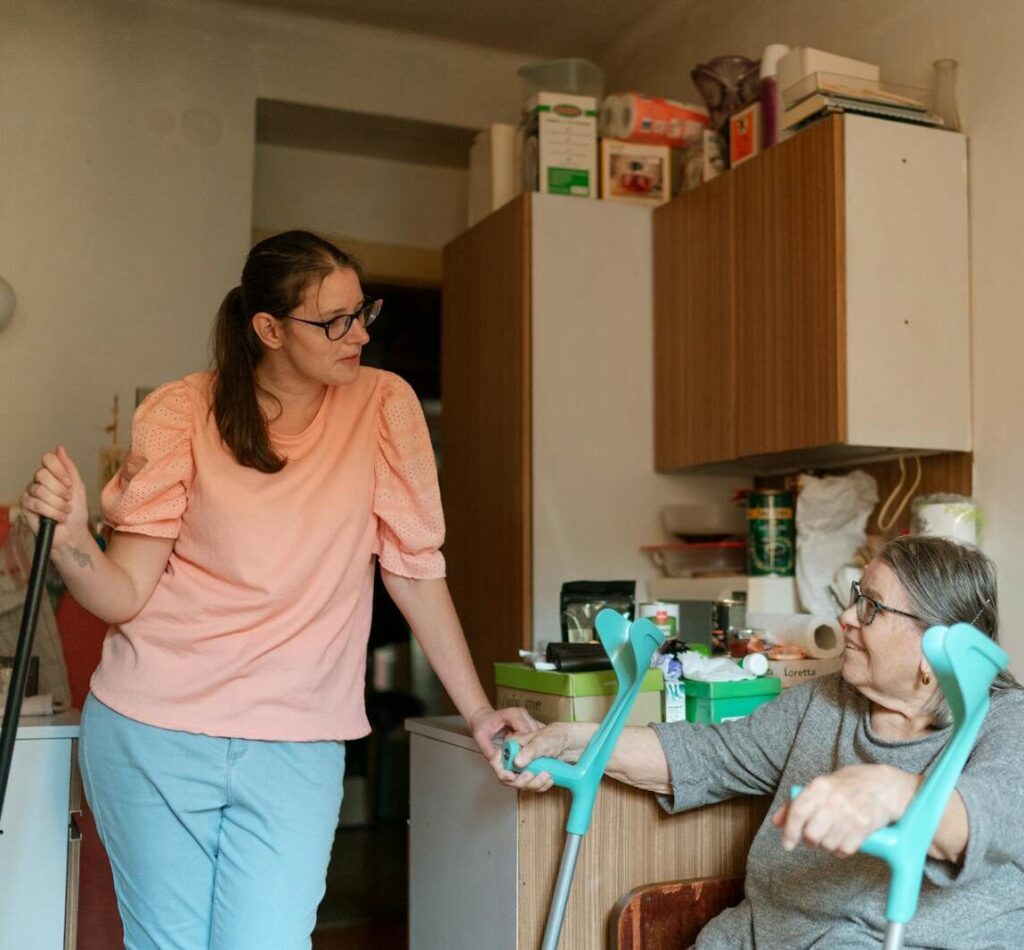 A caregiver engaging with a senior using crutches in a cozy Prague home environment.