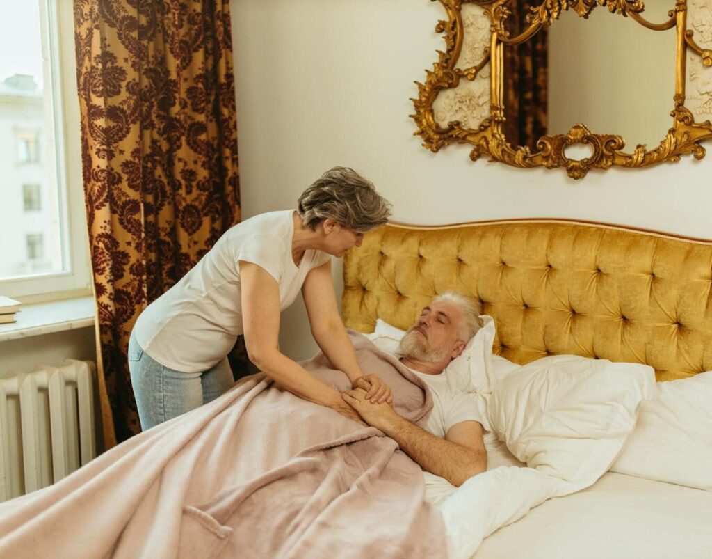 A woman provides comfort to an elderly man lying in bed, showcasing caregiving and family support.